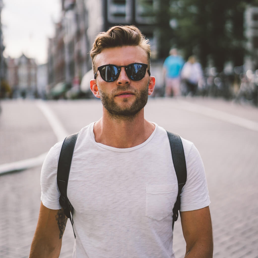 Man wearing sunglasses and a white t-shirt walking on city street.