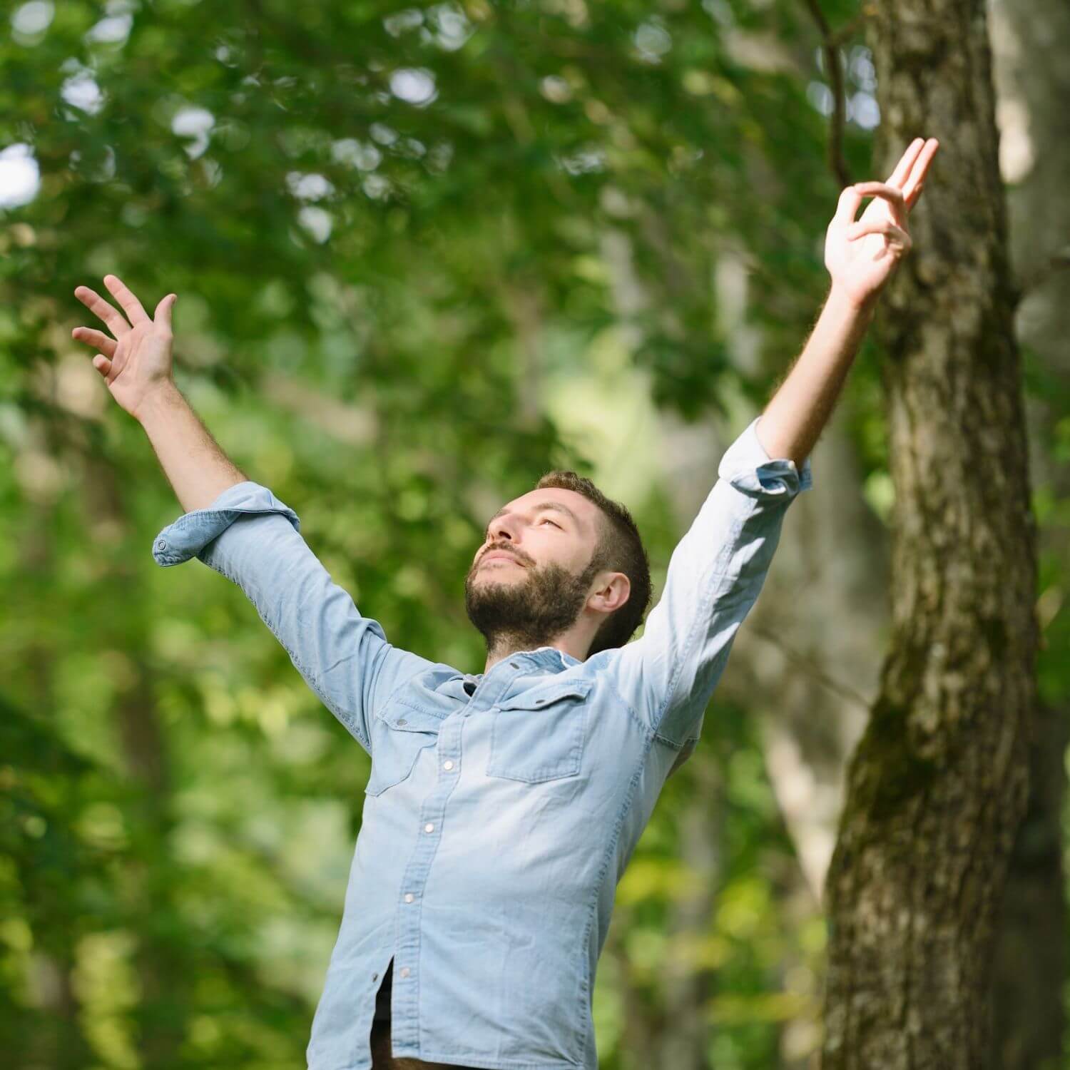 Man enjoying nature with arms raised, expressing joy and freedom in a lush green forest.