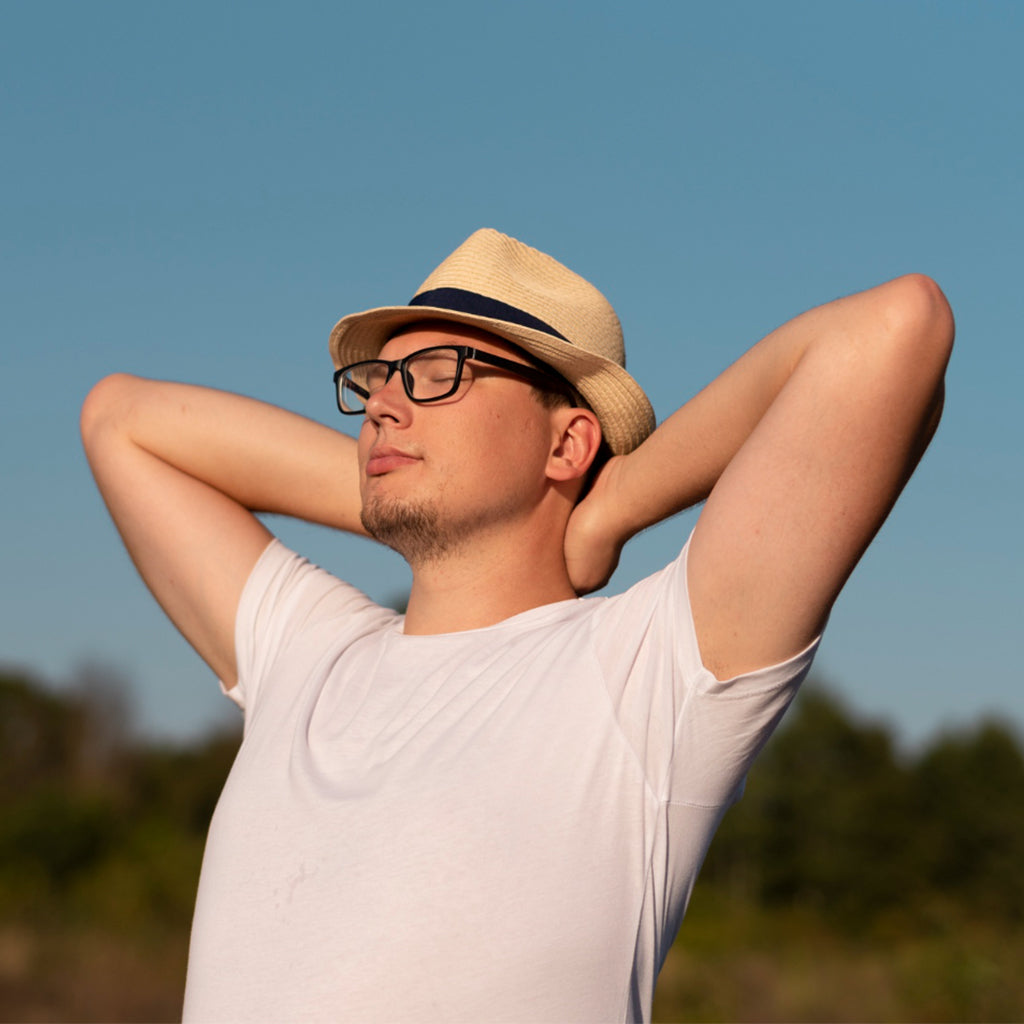 Man enjoying the sun outdoors, wearing a straw hat and glasses while relaxed in a natural setting.