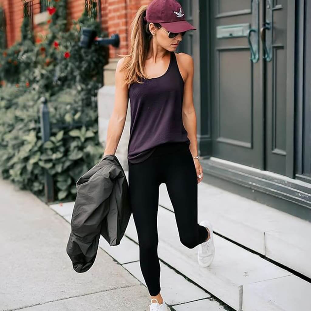 Woman wearing FormFit Leggings with a tank top and cap, walking stylishly in an urban setting.